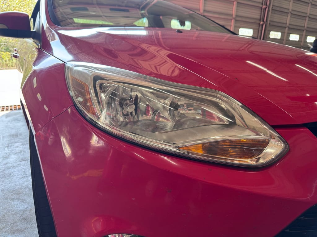 Clear restored headlight on a red vehicle after professional exterior lens service