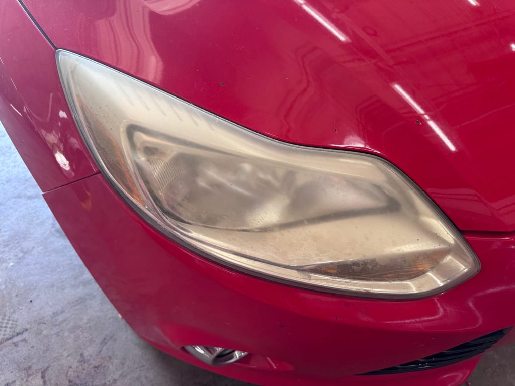 Cloudy headlight on a red vehicle with widespread haze across the exterior lens surface