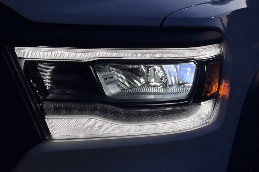 Close-up of an illuminated headlight assembly on a dark blue Ram truck